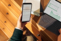 Person holding phone near laptop and tablet on desk